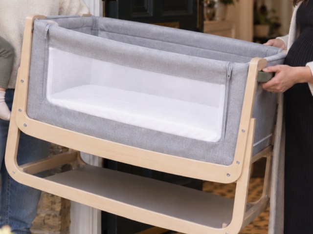 A grey next to me crib with a bent wood frame, held ready to hand over.