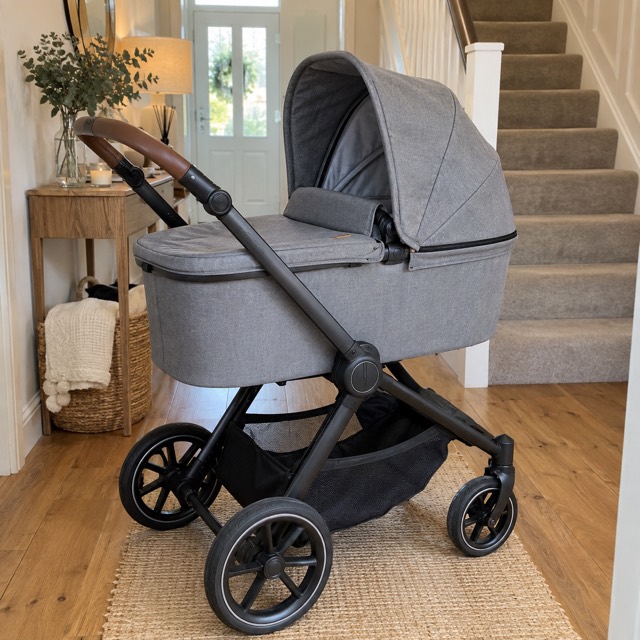 A grey travel system with its carrycot fitted, in a hallway.